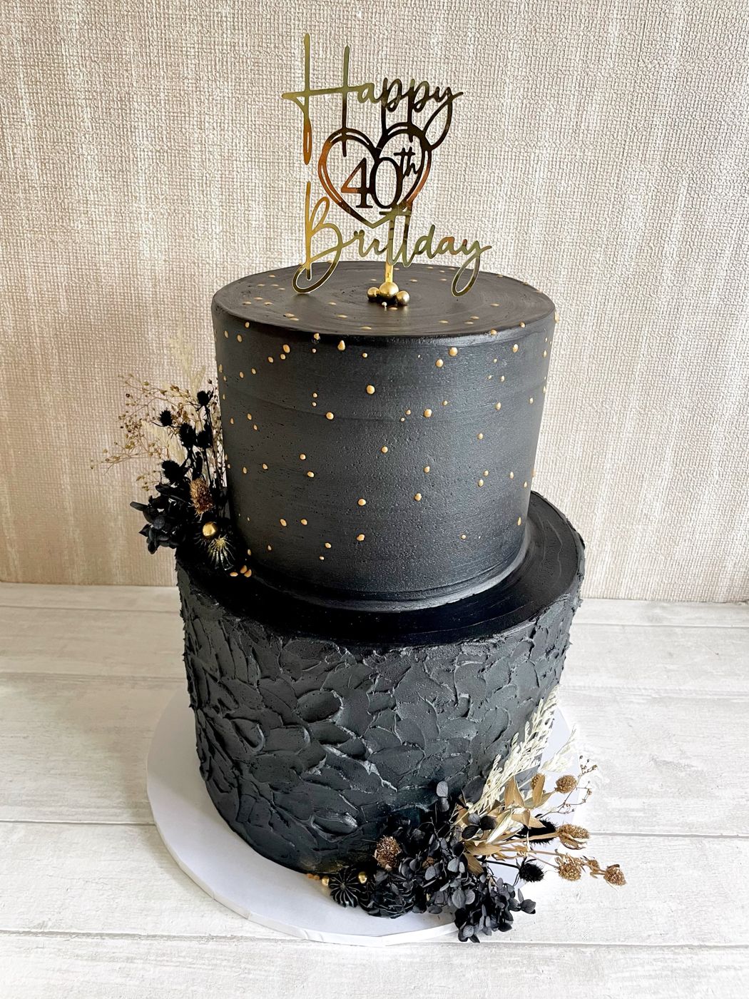 A black and gold 40th birthday cake with dried flowers