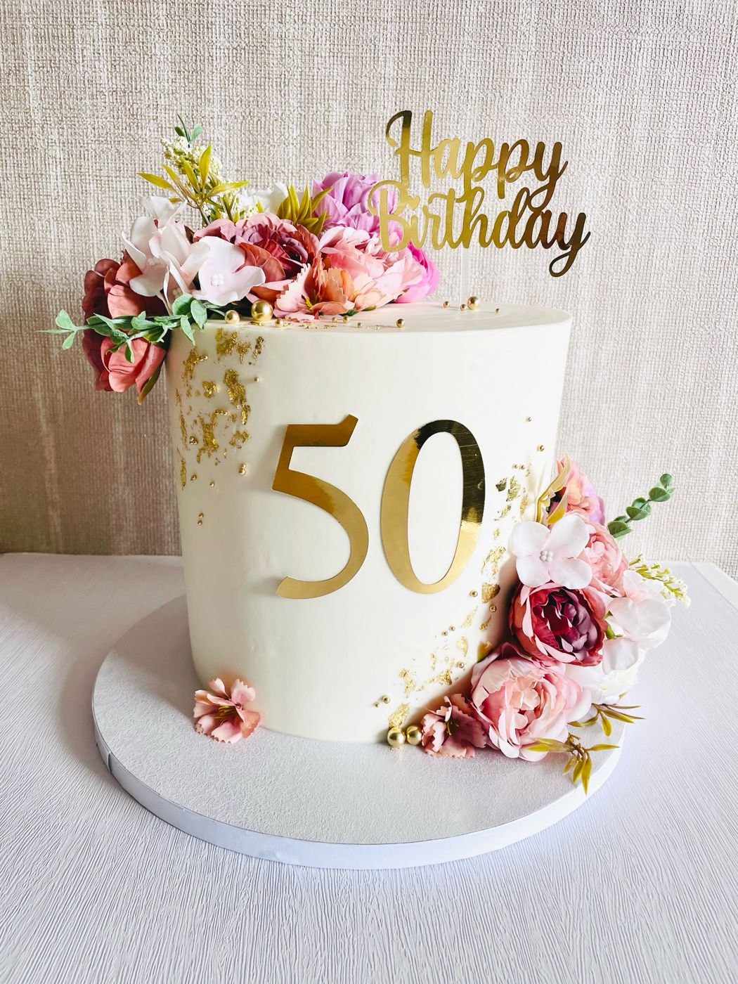 A cream and gold 50th birthday cake with fresh flowers by Cake Me a Cake